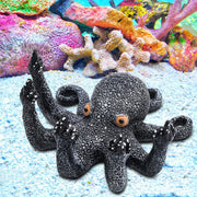 Black textured octopus aquarium ornament with orange eyes sitting on sandy bottom with colorful