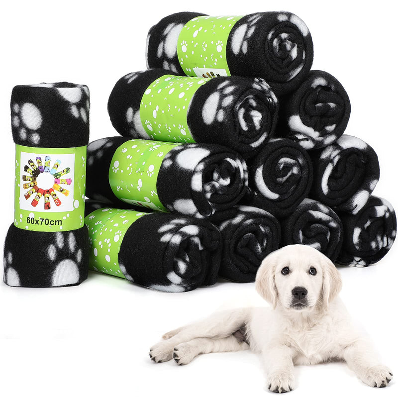 Stack of black and white paw print fleece blankets with green bands next to white puppy