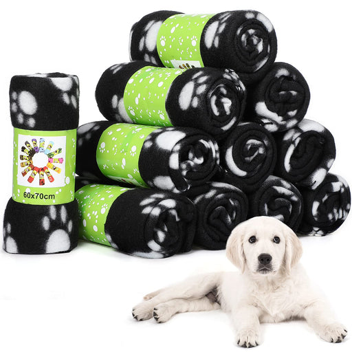 Stack of black and white paw print fleece blankets with green bands next to white puppy