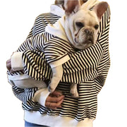 Person holding French Bulldog both wearing matching black and white striped hooded sweatshirts