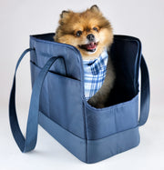 Small Pomeranian dog wearing blue plaid shirt sitting in blue vegan leather pet carrier bag