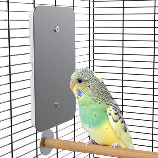 Green and yellow budgie perched on wooden rod next to gray USB heating pad in wire cage