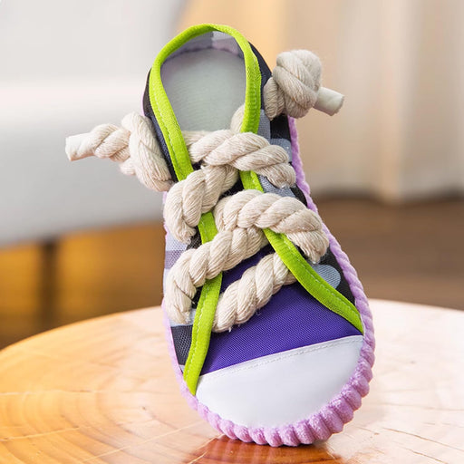 Purple canvas sneaker dog toy with green laces and thick rope tied in knots on wooden surface