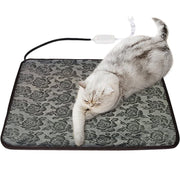 Gray tabby cat lying on floral patterned electric heating mat with USB cord and controller