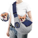Person wearing gray dog sling carrier with navy accents, small chihuahua inside with tongue out
