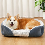 Orange and white Corgi lying in gray and white fluffy rectangular dog bed on wooden floor