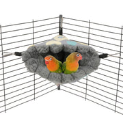 Gray fuzzy bird hammock hanging in cage corner with two orange and green lovebirds snuggled inside