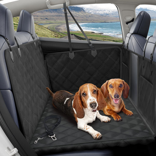 Two dogs sitting on black quilted car hammock with scenic coastal landscape visible through window