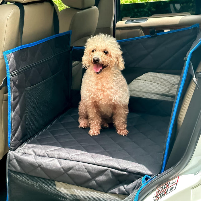 Small poodle sitting in gray quilted car seat extender with blue trim in vehicle back seat