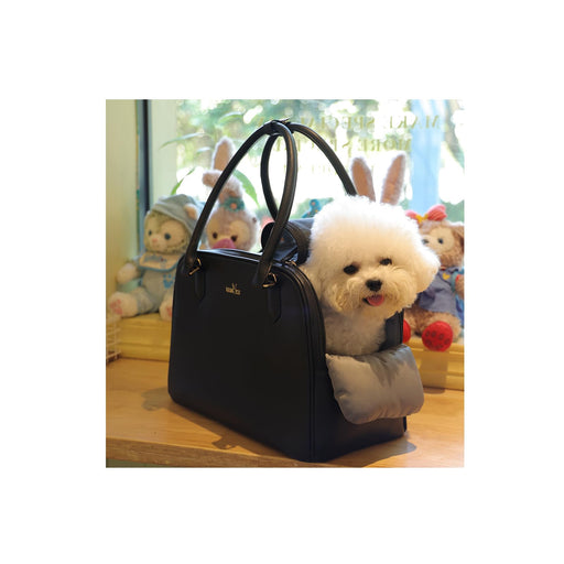 White fluffy dog sitting inside black travel carrier bag with pillow, surrounded by stuffed animals