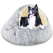 Black and white dog sitting inside gray plush cave-style bed with hood up on white background