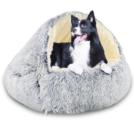 Black and white dog sitting inside gray plush cave-style bed with hood up on white background