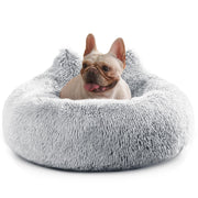 French bulldog sitting comfortably in gray fluffy donut dog bed with tongue out looking happy