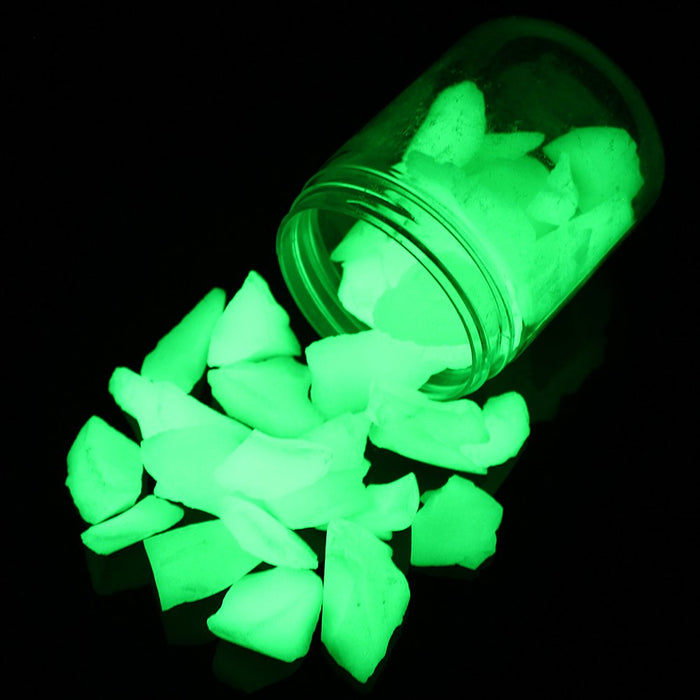 Bright green glowing aquarium stones spilling from glass jar against black background