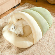 White cat lounging inside a green corduroy and cream fleece slipper-shaped cat cave bed