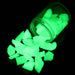 Bright green glowing aquarium stones scattered from glass jar against black background