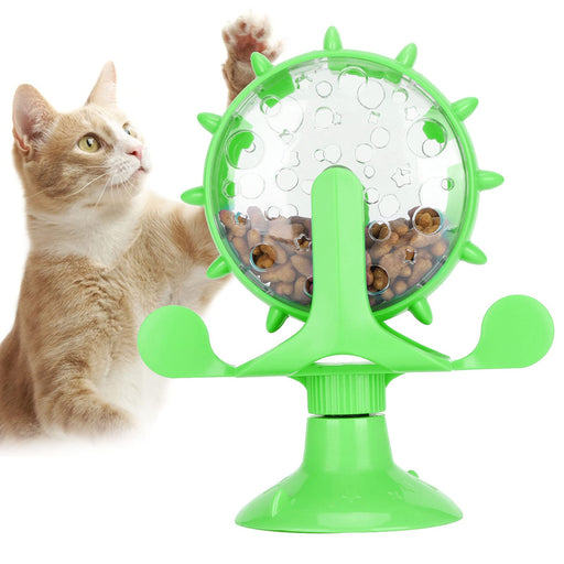 Green windmill-shaped cat puzzle feeder with clear sphere containing kibble and orange tabby cat