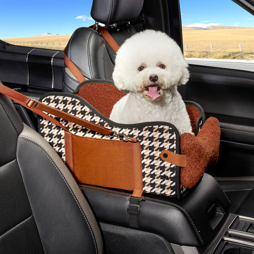 White fluffy dog sitting in brown houndstooth patterned car seat with safety straps in vehicle