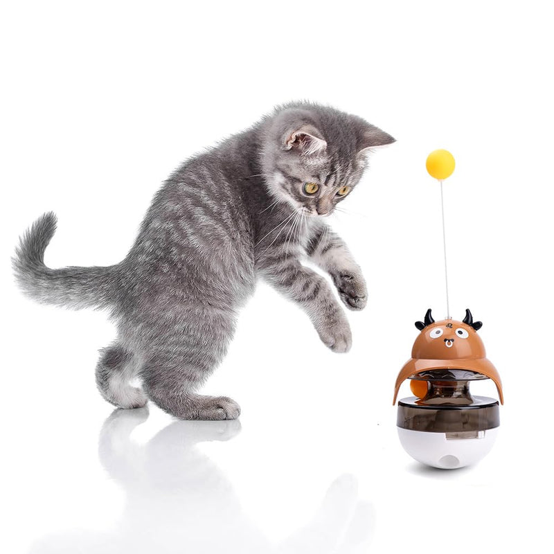 Gray tabby kitten playing with brown cow-shaped interactive treat dispenser with yellow ball on top