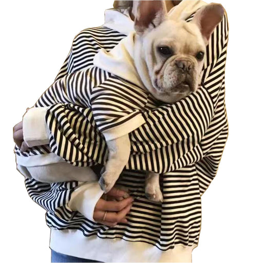Person holding French Bulldog both wearing matching black and white striped hooded sweatshirts