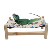 Green iguana resting on natural wood hammock bed with patterned fabric sling