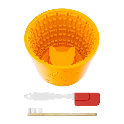 Orange silicone slow feed dog bowl with textured interior and cleaning tools on white background