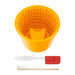 Orange silicone slow feed dog bowl with textured interior and cleaning tools on white background