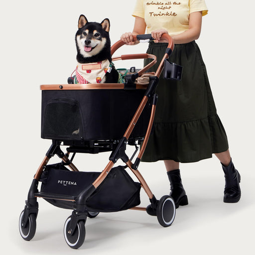 Black Shiba Inu dog sitting in pet stroller with rose gold frame, person pushing from behind