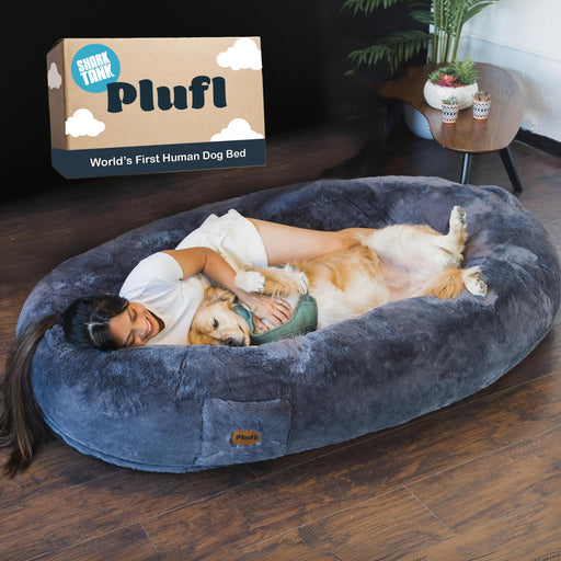 Woman cuddling with golden retriever in large gray fuzzy human dog bed next to product box