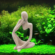 Sandstone thinker statue sitting cross-legged in planted aquarium with green plants and small fish