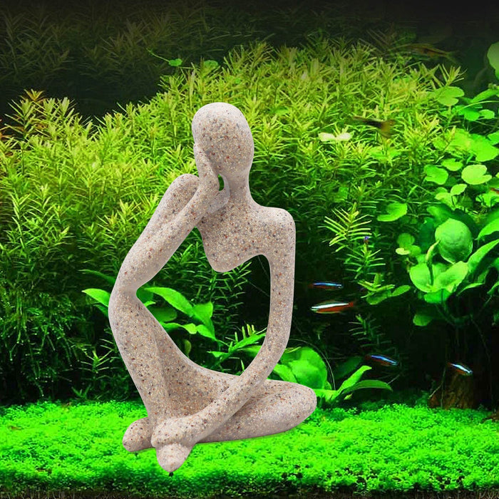 Sandstone thinker statue sitting cross-legged in planted aquarium with green plants and small fish