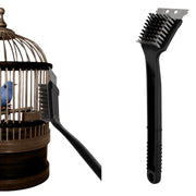 Black stainless steel bird cage cleaning brush with wire bristles next to wooden birdcage
