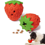 Two red strawberry puzzle toys with green tops, kibble scattered, and black and white puppy playing