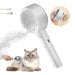 White handheld pet grooming brush with steam feature and metal pins, shown with fluffy cat