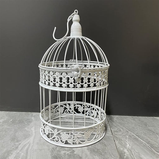 White decorative iron bird cage with ornate floral patterns and dome top on gray surface