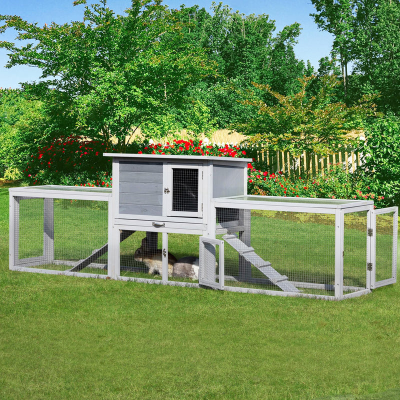Gray wooden rabbit hutch with attached run on green lawn in garden setting with flowers