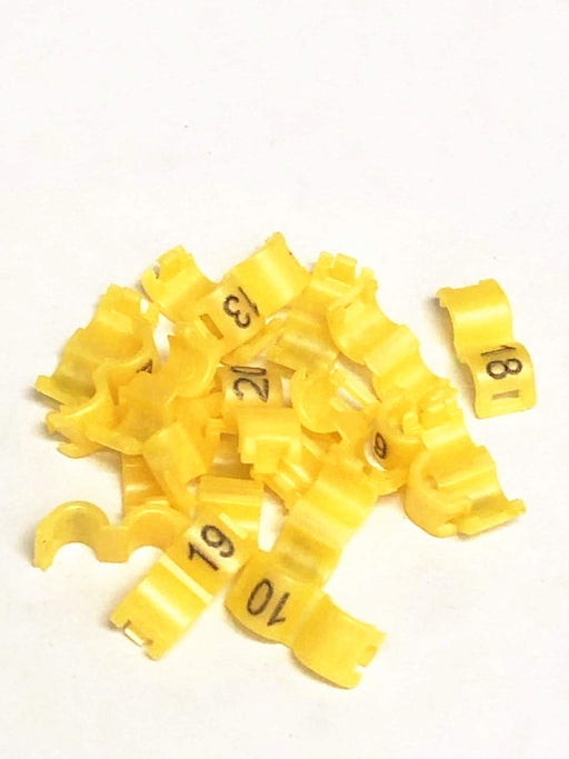 Yellow plastic bird leg bands with black numbers scattered on white background
